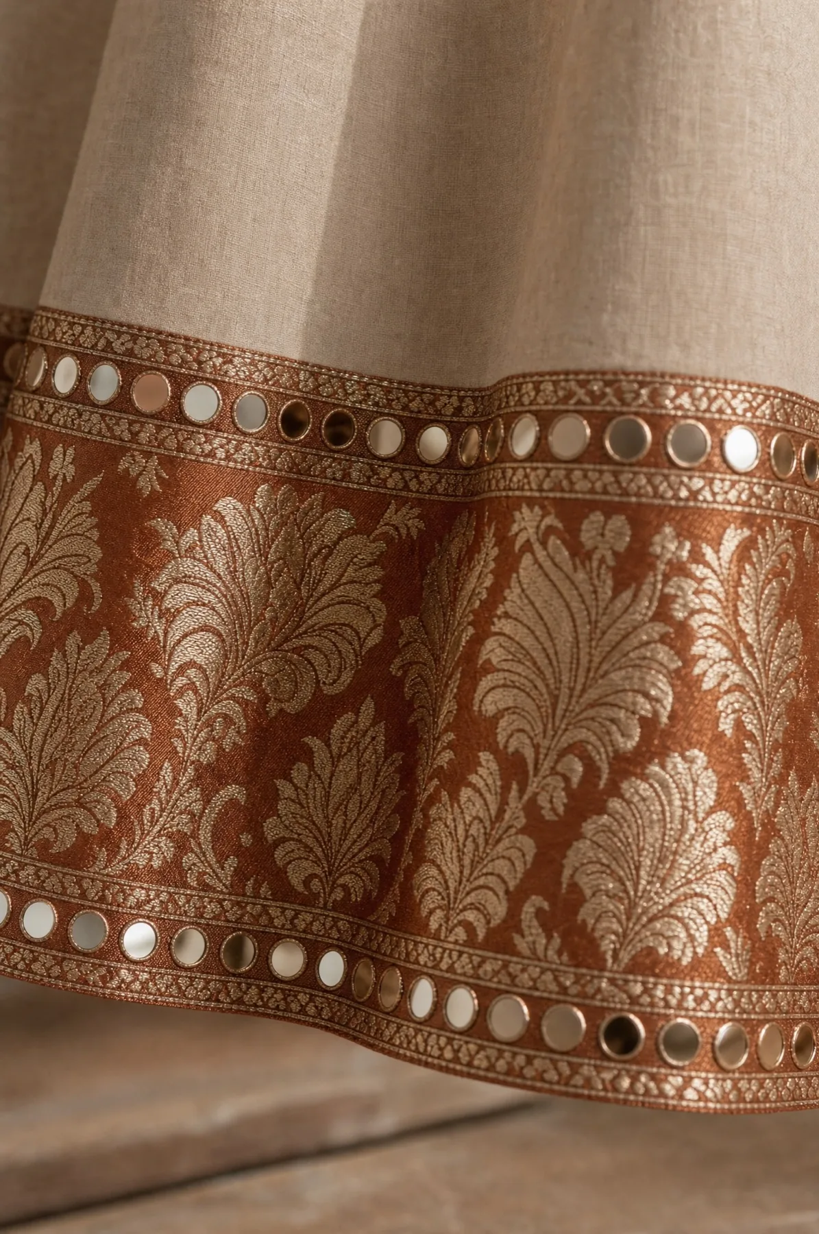 Close view of a hem border in copper brocade, edged above and below with rows of round mirrors in gold rings.